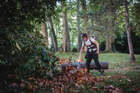 Un jeune en formation jardinier paysagiste en train de souffler les feuilles 