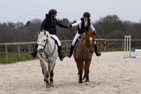 2 jeunes à cheval se tiennent la main dans une carrière